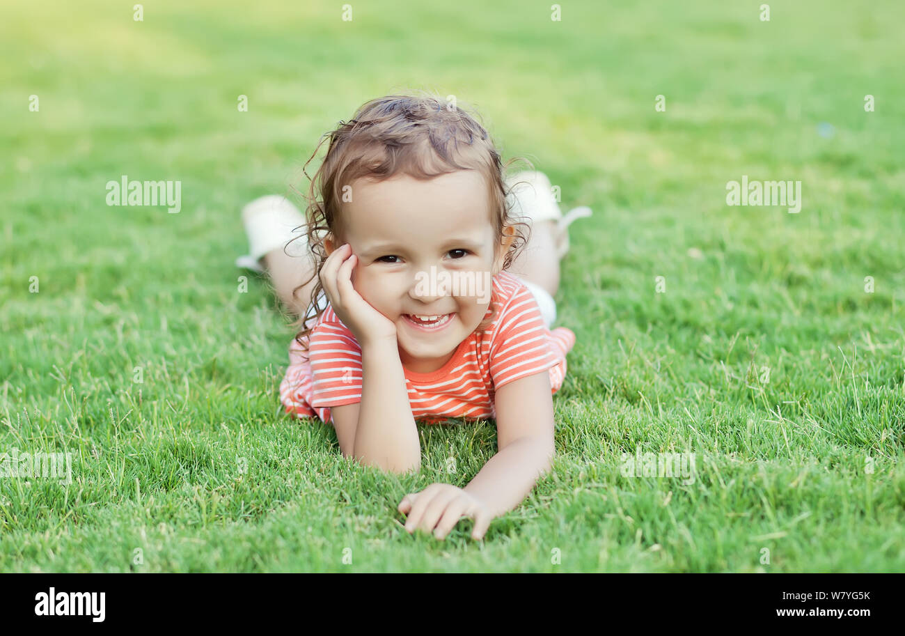 Portrait of a smiling little girl lying on green grass Stock Photo - Alamy