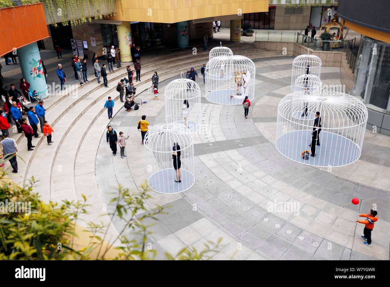 Artists wearing wings are confined in huge bird cages during a flash mob to call for citizens to extricate themselves from city life at Golden Hongqia Stock Photo