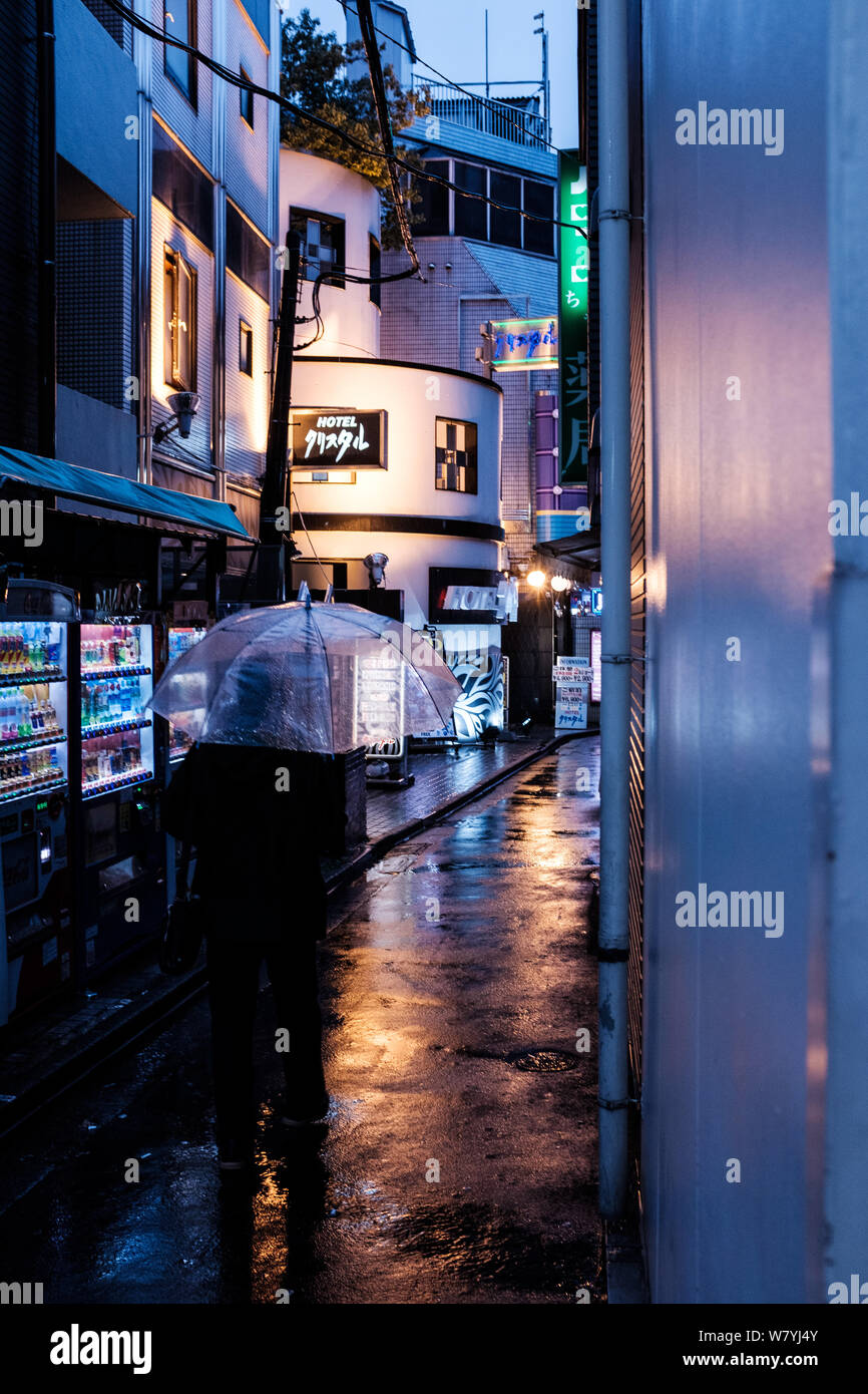 Man holding umbrella walks down a rainy street in Tokyo, Japan Stock Photo