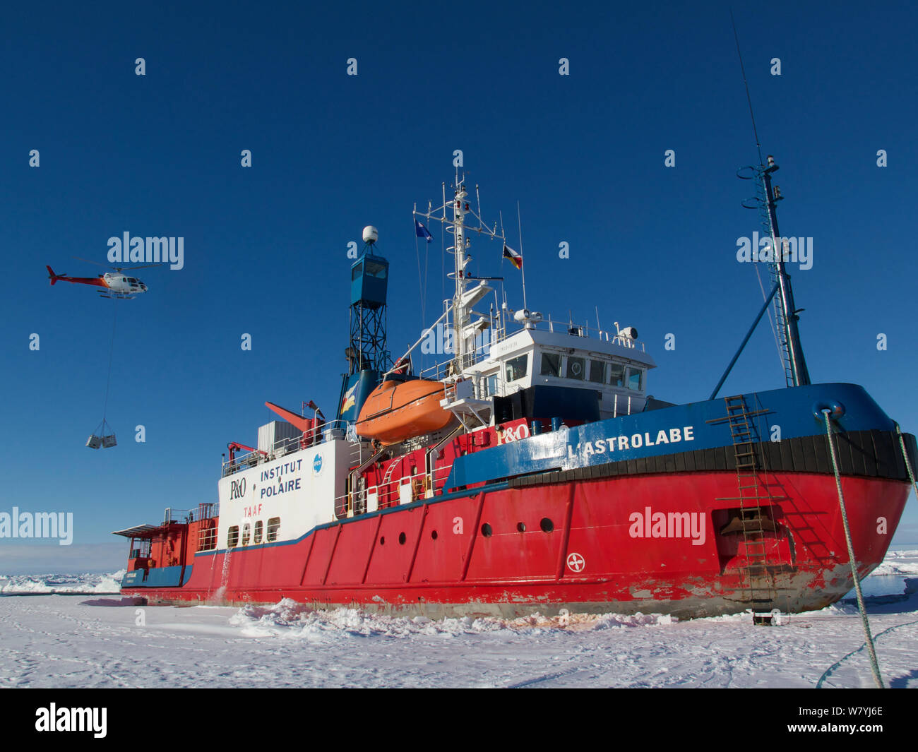 French Icebreaker L&#39;Astrolabe on the edge of the fast ice off Dumont D&#39;Urville station, with helicopter moving supplies onto the ship. Antarctica. December 2014. Stock Photo
