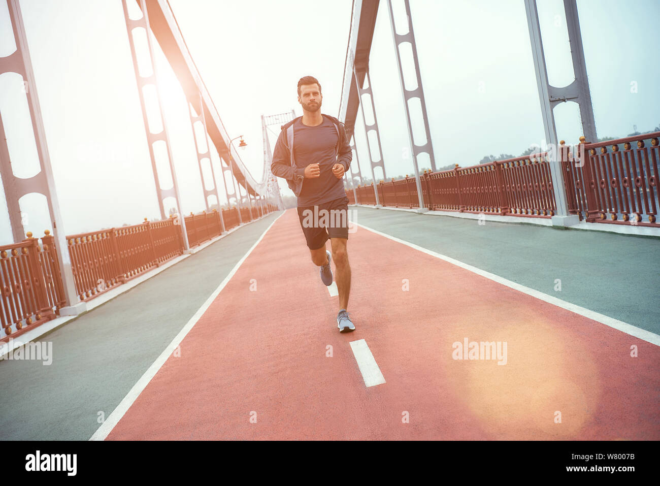 Never give up Full length of young and handsome bearded man in sports clothing jogging on the bridge in the morning. Sport concept. Healthy lifestyle. Exercising Stock Photo
