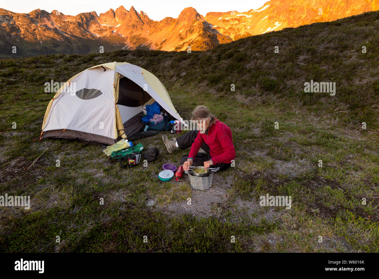 Woman cooking next to tent, Miners Ridge, Glacier Peak Wilderness, Wenatchee National Forest, Washington, USA. Model released. Stock Photo