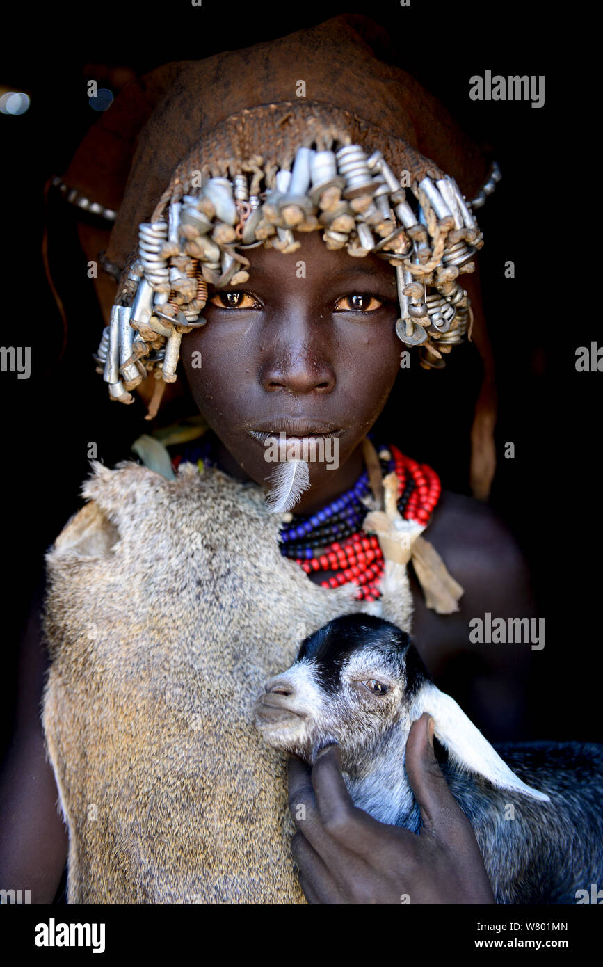 Dassanech girl with headdress of nuts and bolts, holding goat, Dassanech tribe, Lower Omo Valley. Ethiopia, November 2014 Stock Photo