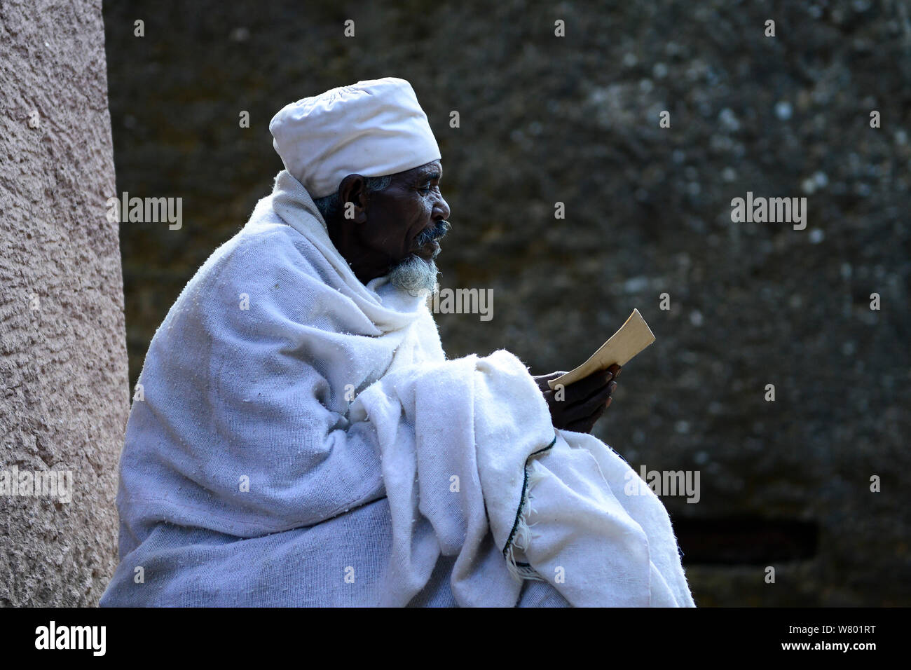 Devout Christian in traditional robes studying at Bet Medhane Alem (part of the northwestern group of churches in Lalibela). UNESCO World Heritage Site. Lalibela. Ethiopia, December 2014. Stock Photo