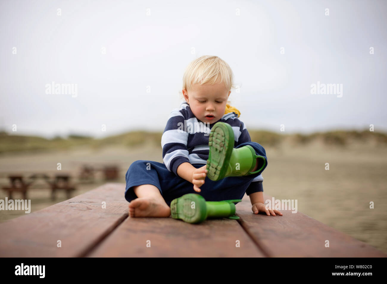Toddler taking off rubber boots outside Stock Photo Alamy