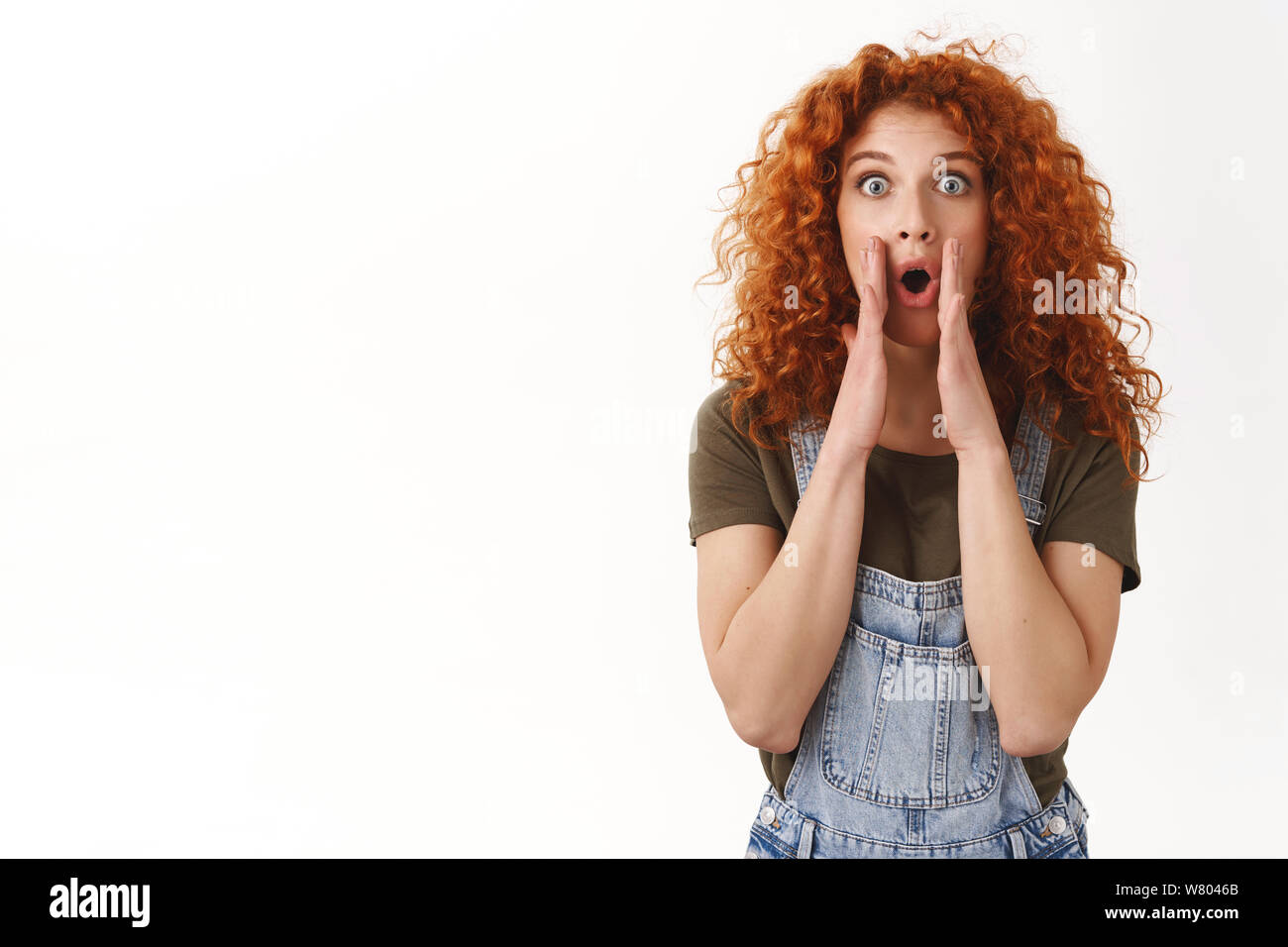 Alert amazing news, hear me out. Astonished excited curly-haired ginger girl popping eyes camera excited, hold hands near opened mouth to shout out lo Stock Photo
