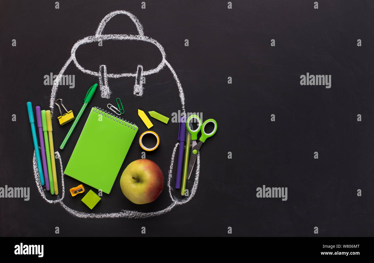 Green school stationery inside chalk painted backpack on black Stock Photo