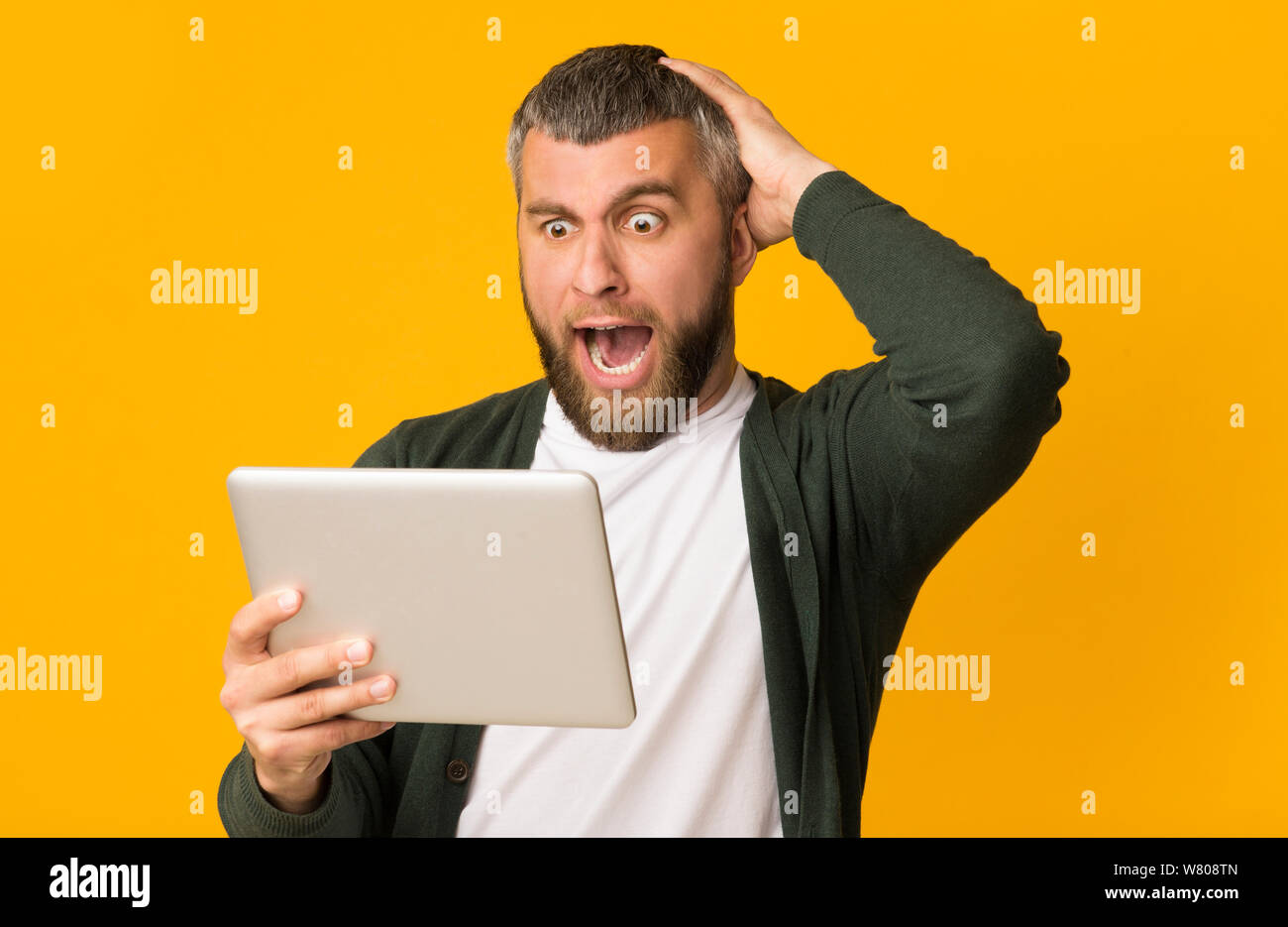 Impressed bearded man holding tablet and touching his head Stock Photo