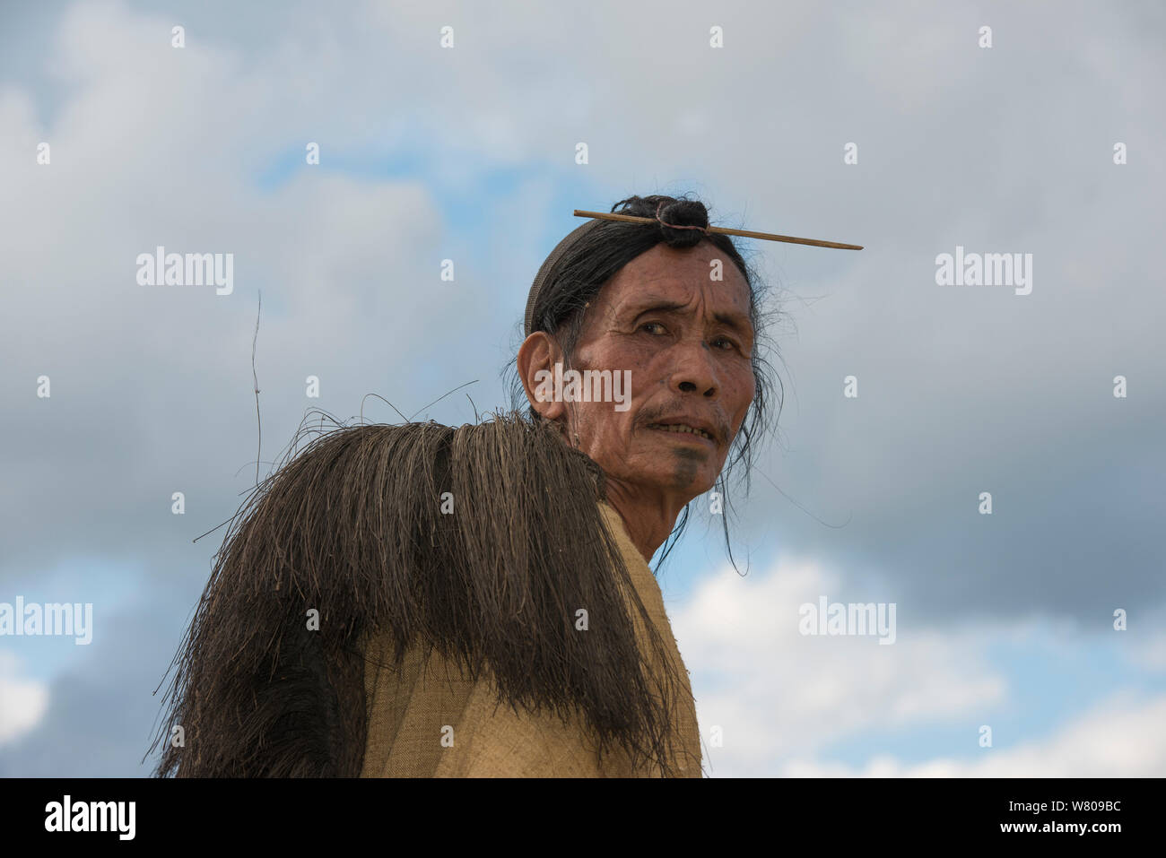 Apatani man with traditional hair knot fixed by a skewer or Piidin Khotu and traditional Lecha over shoulder and cane hat which includes a hornbills beak. Apatani Tribe, Ziro Valley, Himalayan Foothills, Arunachal Pradesh.North East India, November 2014. Stock Photo