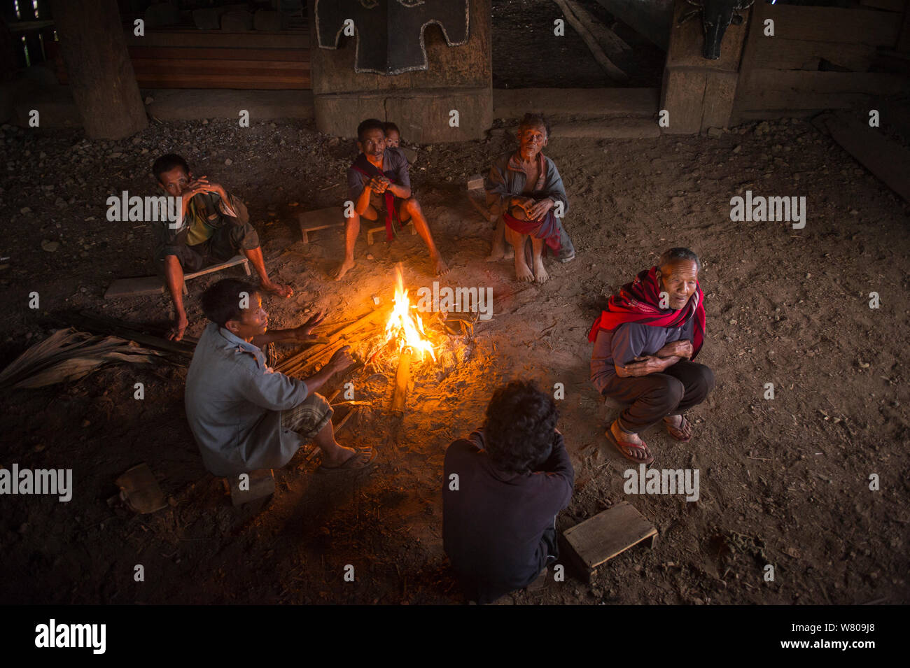 Men sitting around fire in Konyak Naga Morong or communal house. Mon district, Nagaland, North East India, October 2014. Stock Photo