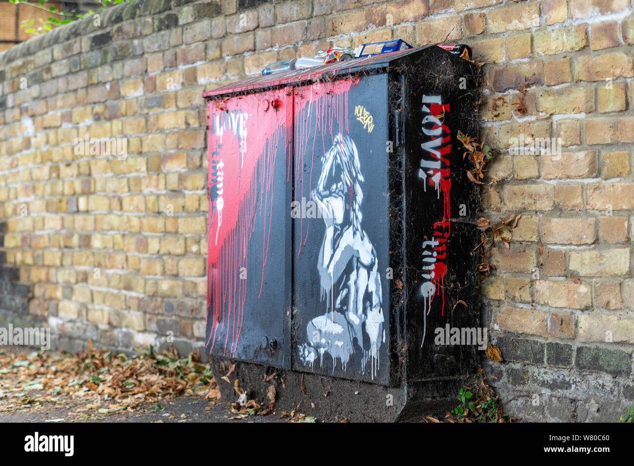 Banksy style artwork of a crying child on a telecommunications junction box, with red paint running down like blood and the words Love Time. Rubbish Stock Photo