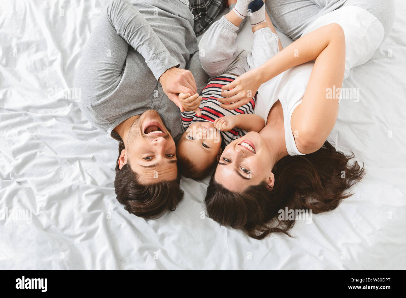 Young man, woman and baby cuddling in bed together Stock Photo