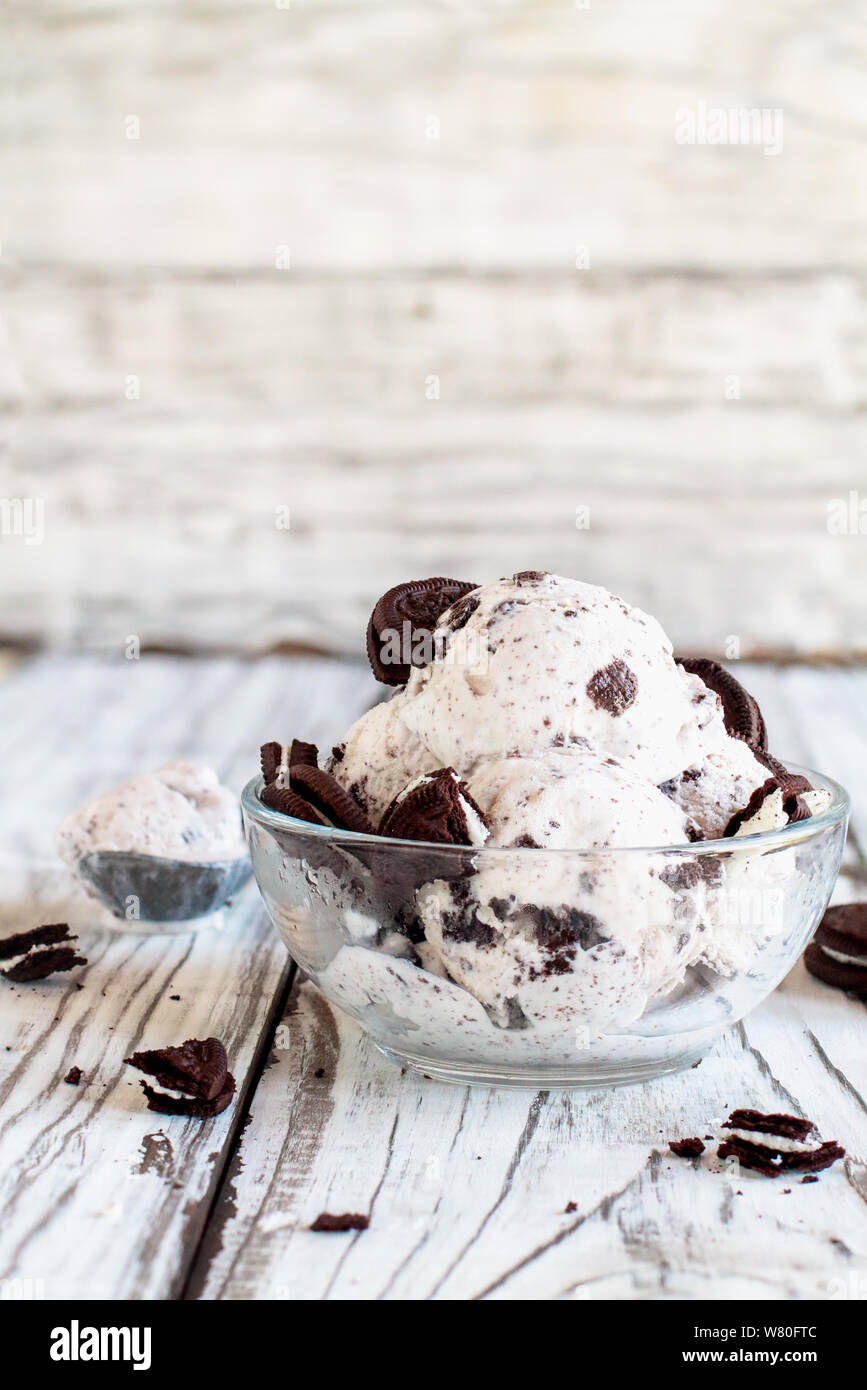 Clear glass bowl of cookies and cream ice cream. Selective focus with blurred background. Whole and crumbled cream filled cookies scattered about tabl Stock Photo