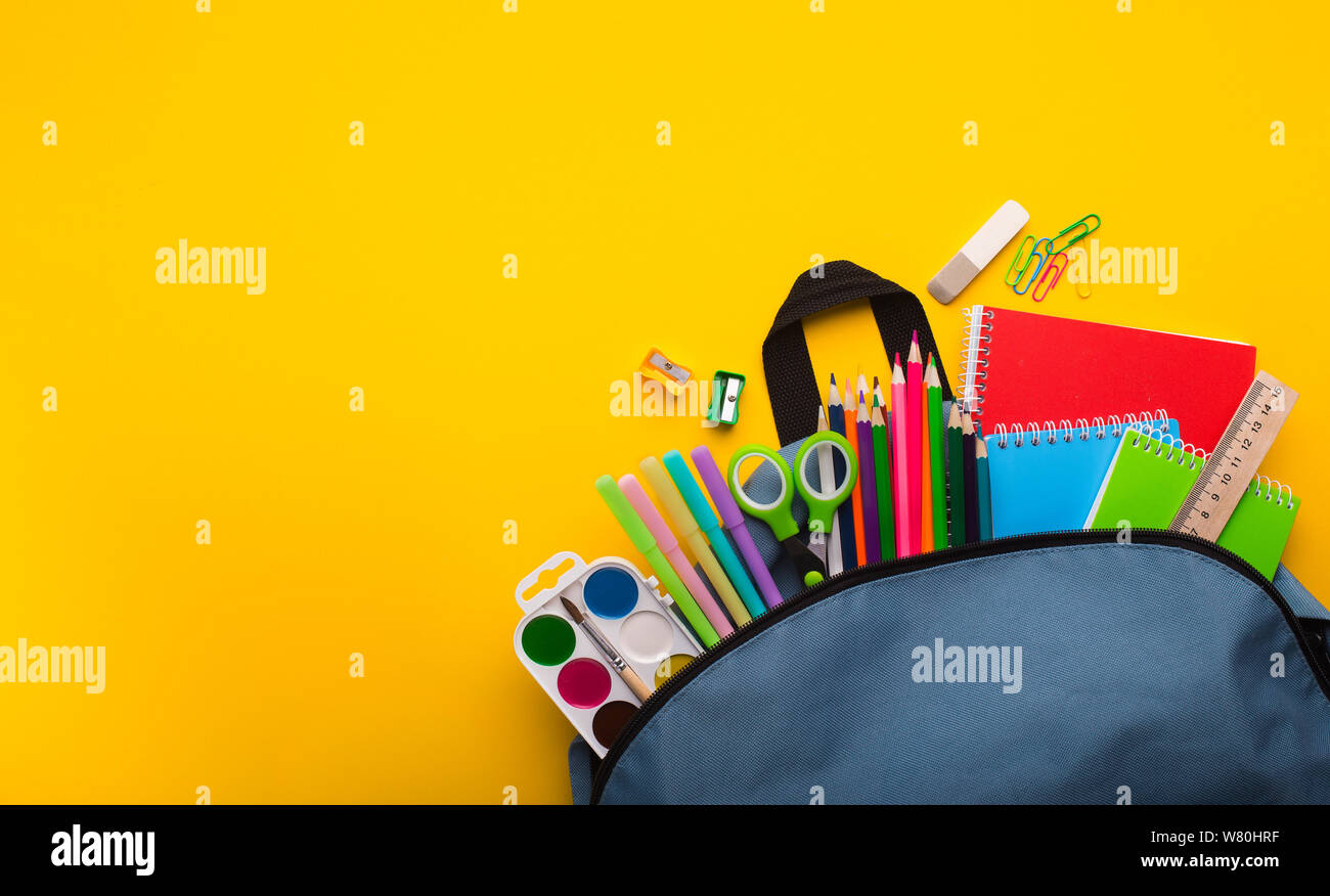 Backpack with stationery inside on yellow background Stock Photo