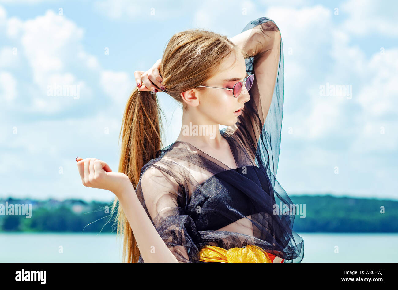 Young girl in red sunglasses posing over sky background, bright