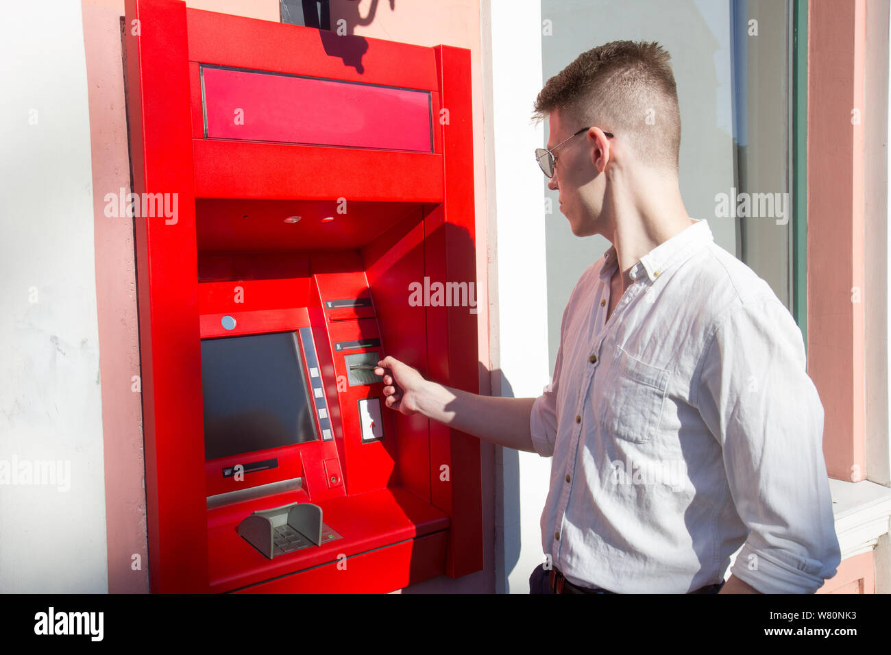 young man student withdrawing money from a bank cash point, outdoors Stock Photo