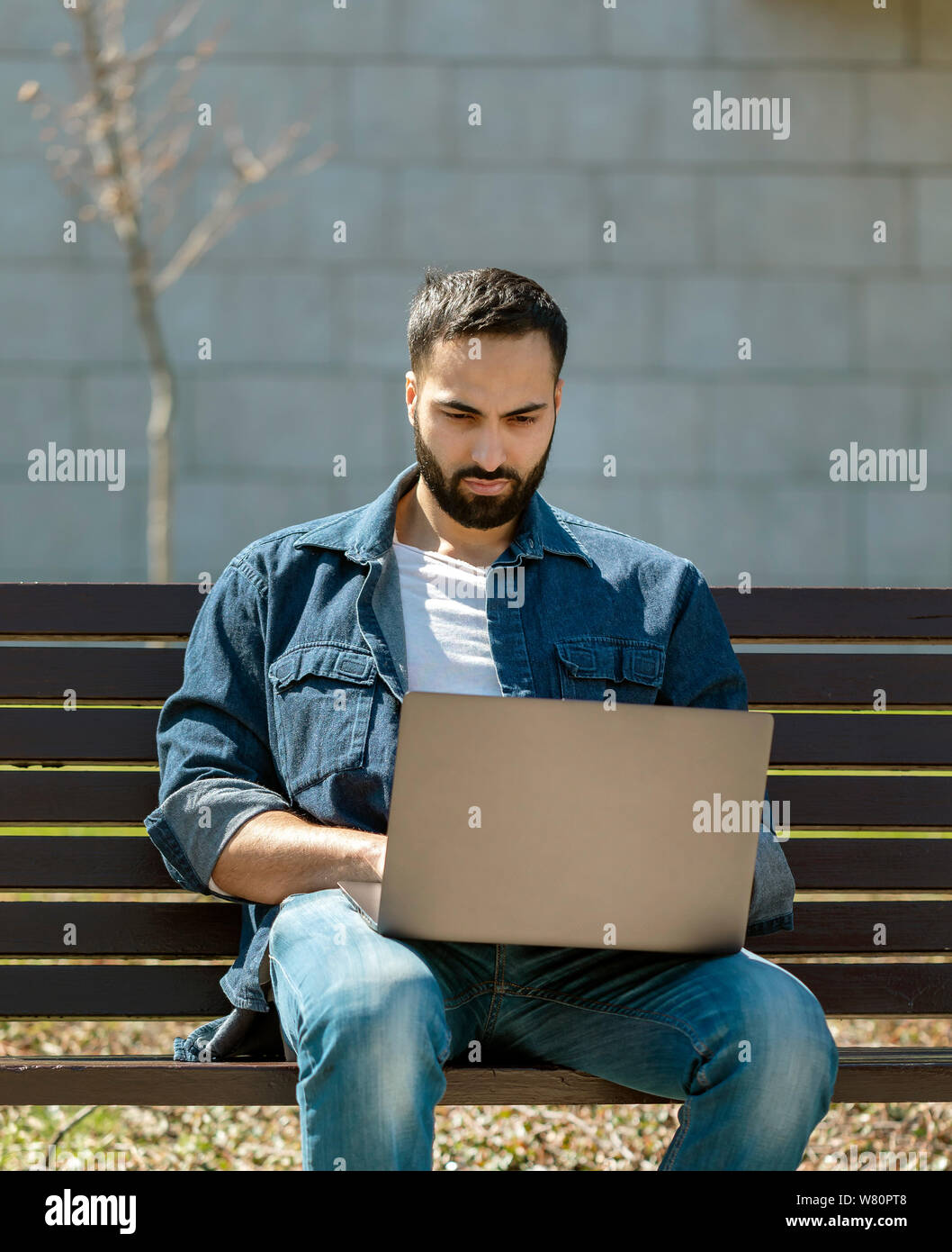 Handsome young manager working on laptop while sitting outdoors on the bench, concept of work life balance Stock Photo
