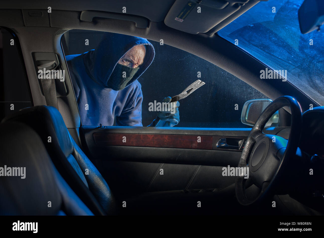 Robber and thief trying to break into a car for it's contents Stock Photo