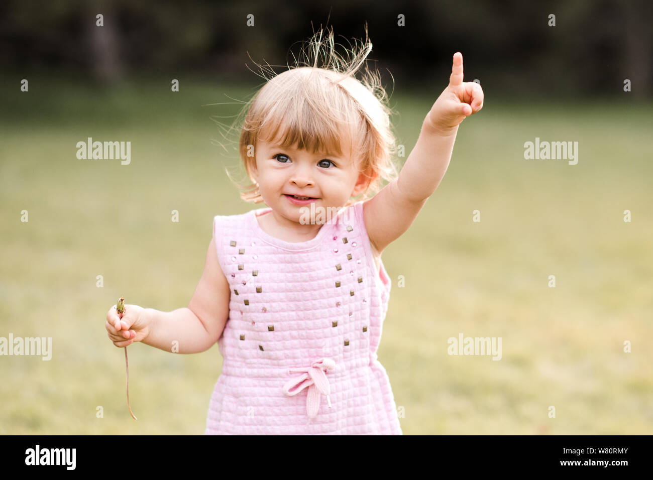 Pretty baby girl 1-2 year old showing up something with finger outdoors closeup. Childhood. Happiness. Stock Photo