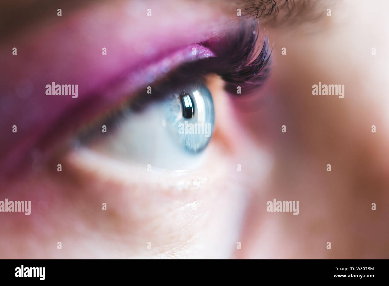 Open blue eye with pink eyeshadow and mascara closeup. Selective focus. Stock Photo