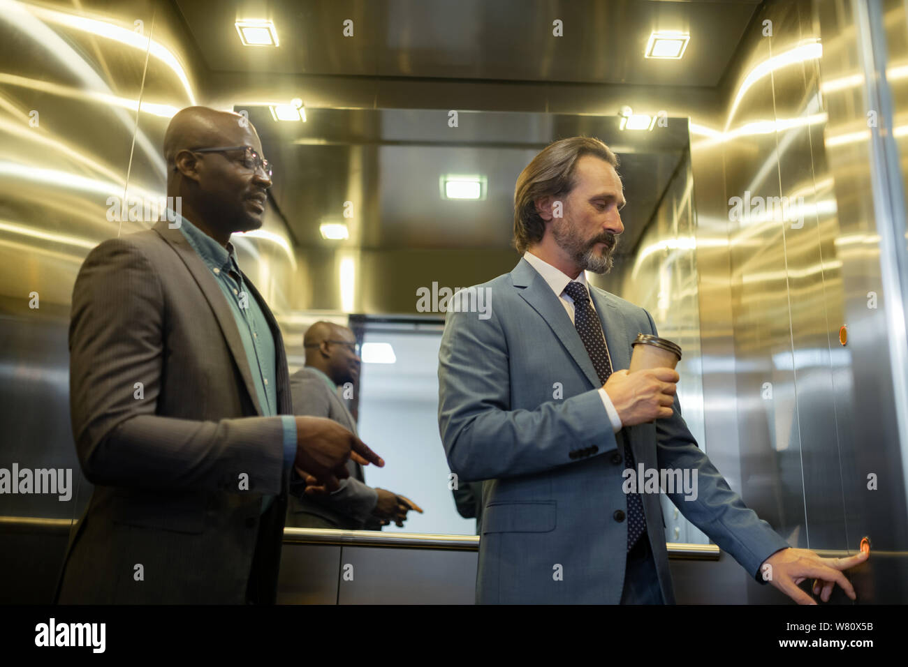 Grey-haired mature businessman pressing button in elevator Stock Photo
