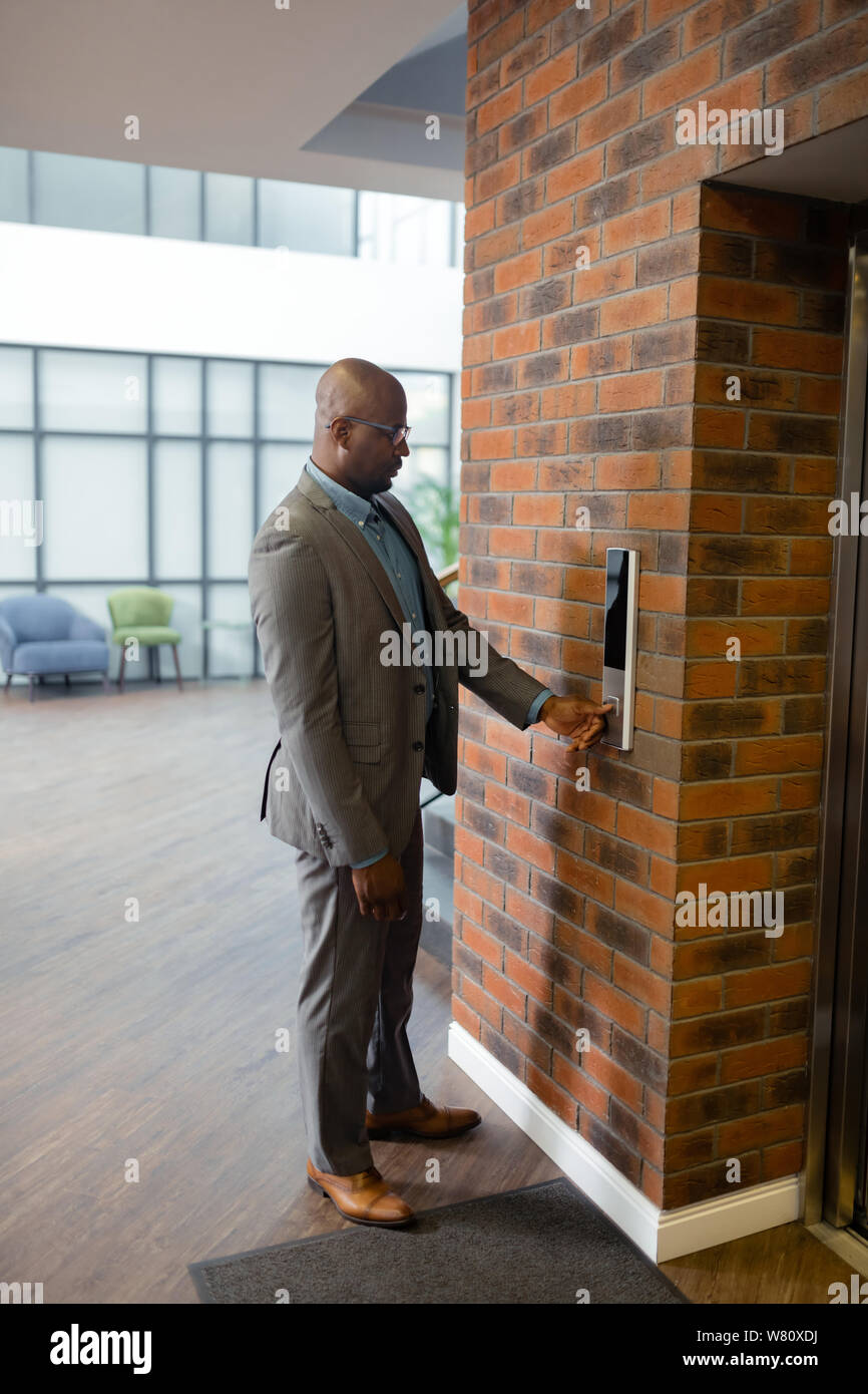 Dark-skinned businessman pressing button while waiting for elevator Stock Photo