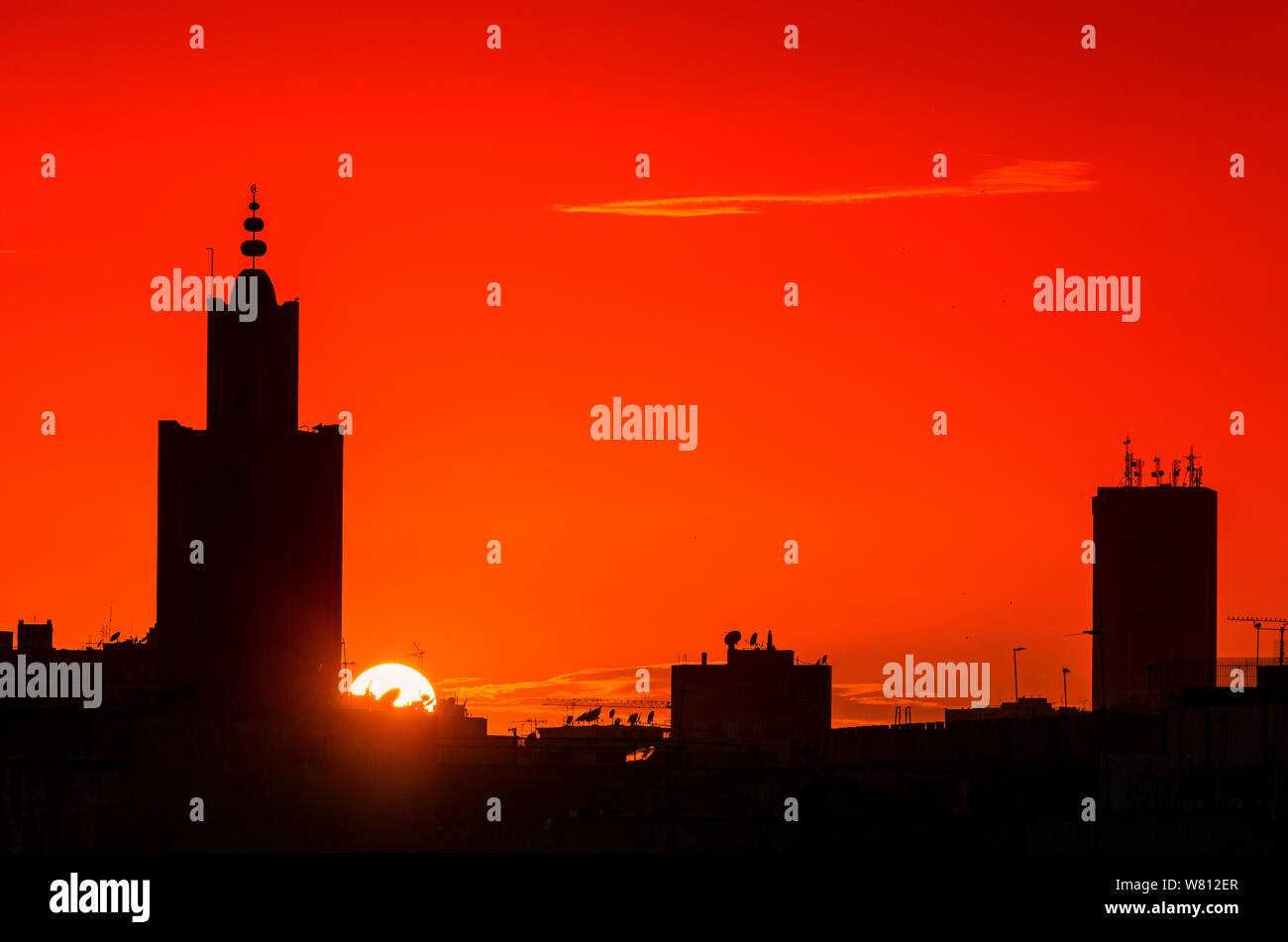 Sunset over the city, a mosque and buildings in silhouette on a background of orange sky. Stock Photo