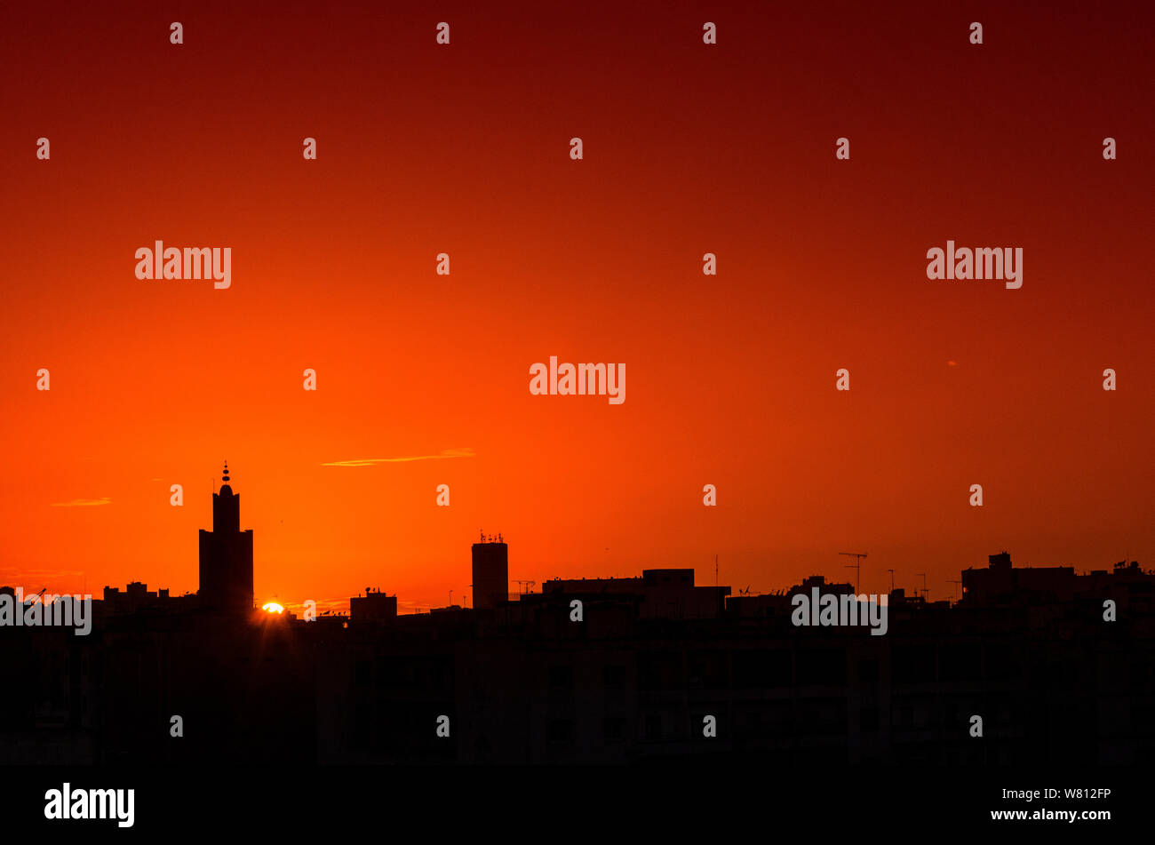 Sunset over the city, a mosque and buildings in silhouette on a background of orange sky. Stock Photo