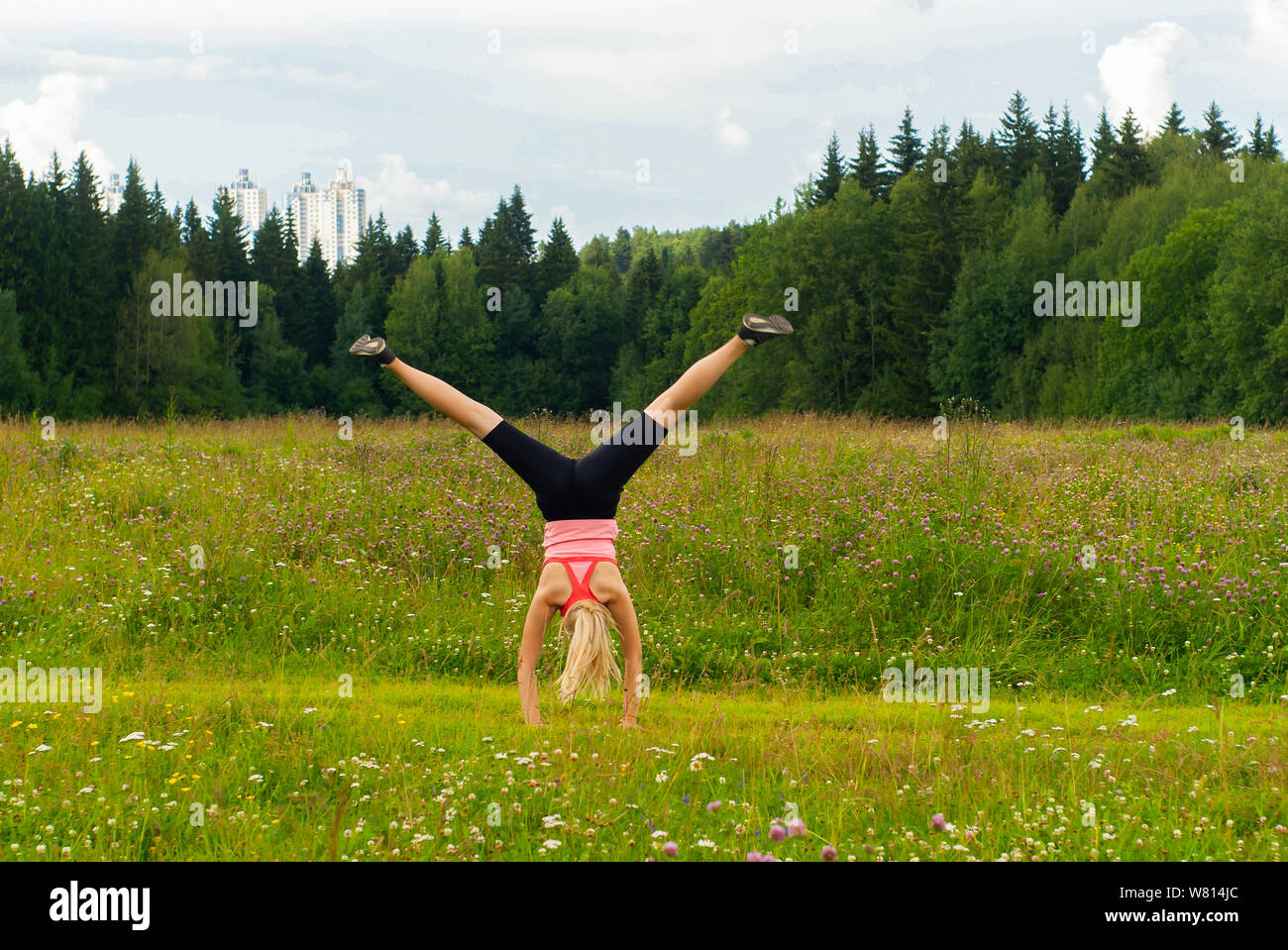 young woman doing somersault cartwheel outdoors in a meadow outside the city Stock Photo