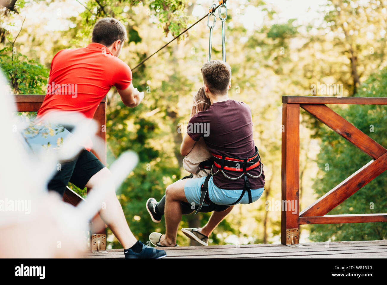 Back view of a rope slide worker pushing a couple over the rope slide ...