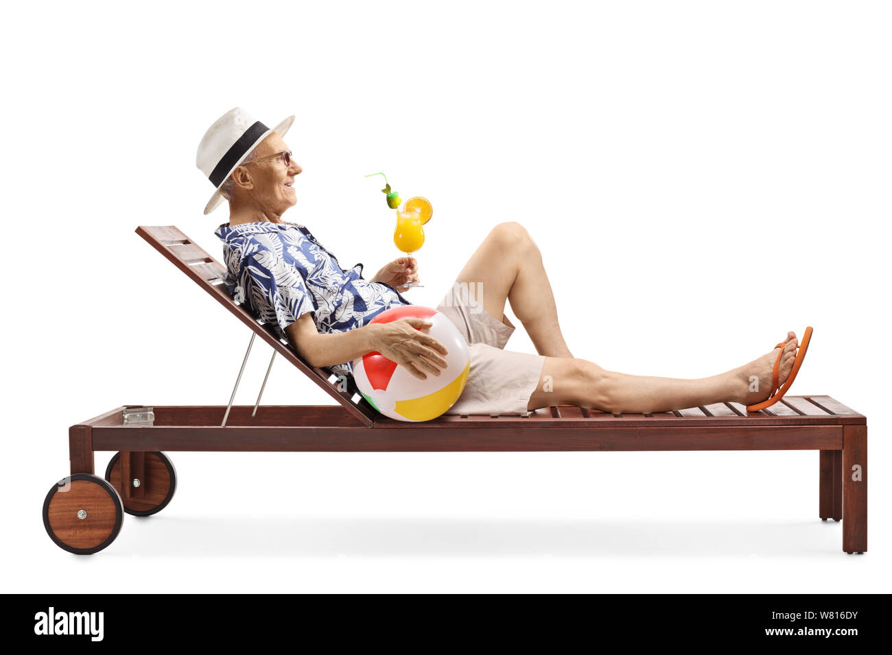 Full length profile shot of an elderly man lying on a sunbed drinking a cocktail and holding an inflatable beach ball isolated on white background Stock Photo