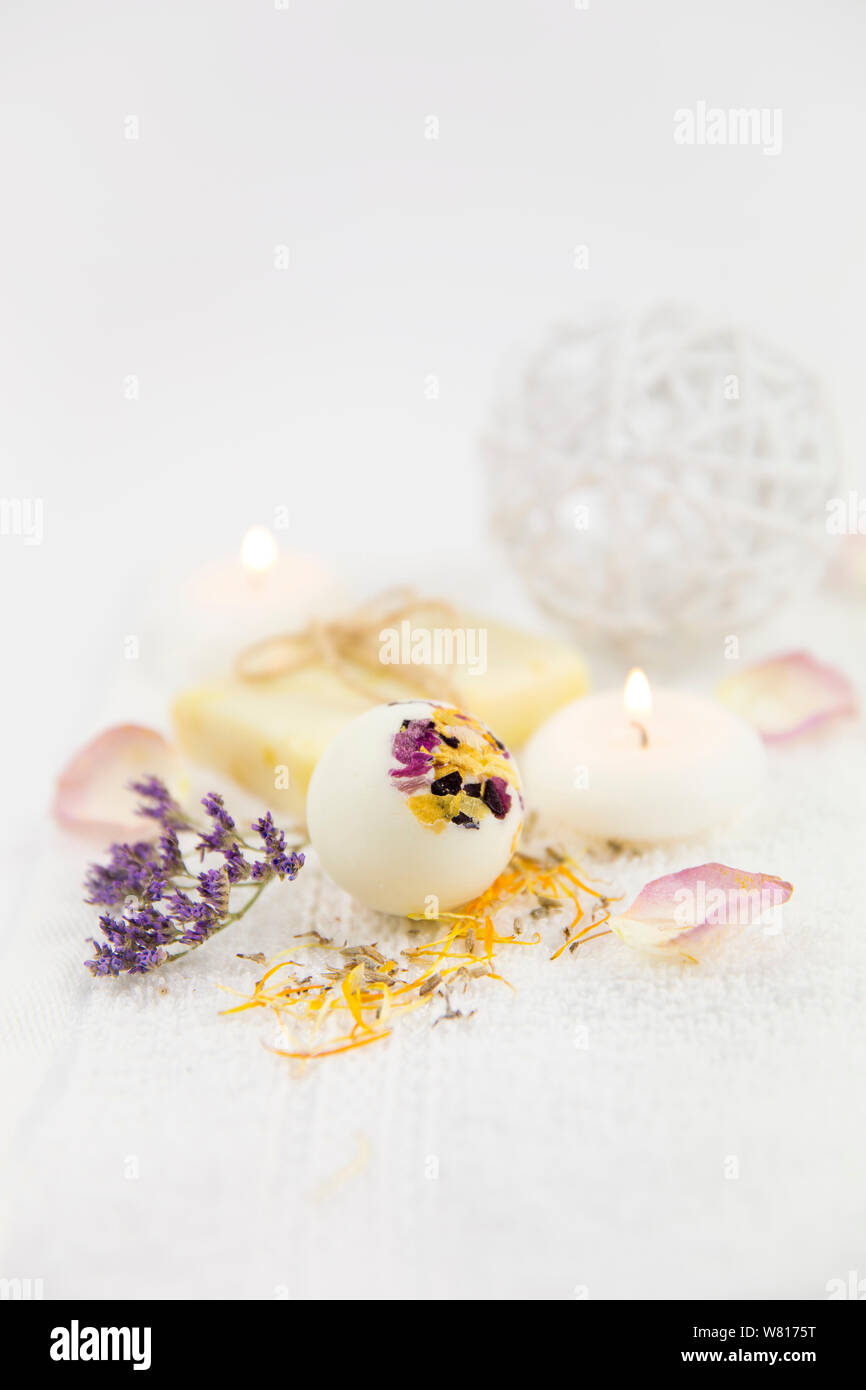Beautiful set with selective focus on white creamy moisturizing small bath ball bomb with dry flower blossom petals, spa candles burning and dry flowe Stock Photo