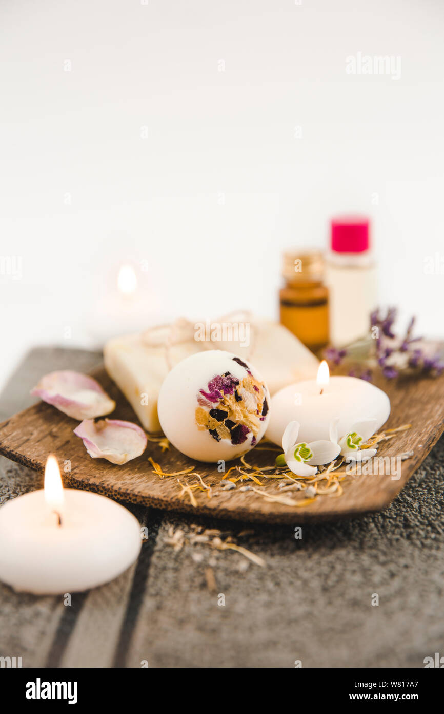 Various spa bath products on brown wooden tray creamy bath bomb, natural soap bar with cotton string, dried flower petals, spa candles lit, essential Stock Photo