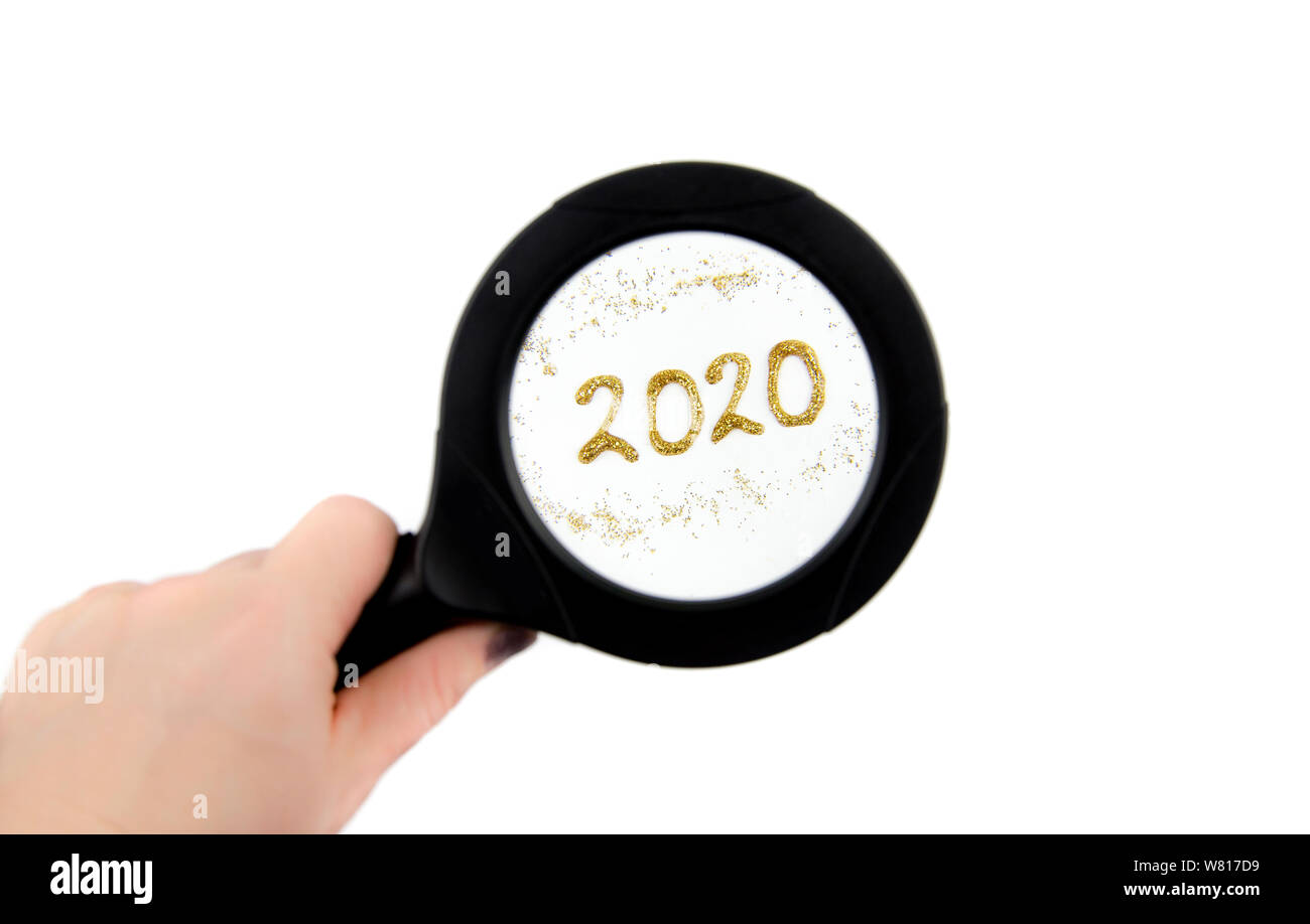 Hand holding magnifying glass and looking through, seeing year 2020 text. New year concept. Stock Photo