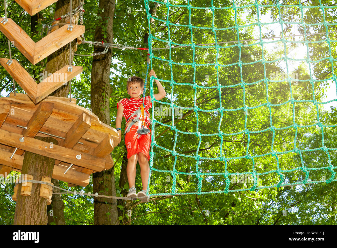Boy climb from platform to net between trees Stock Photo