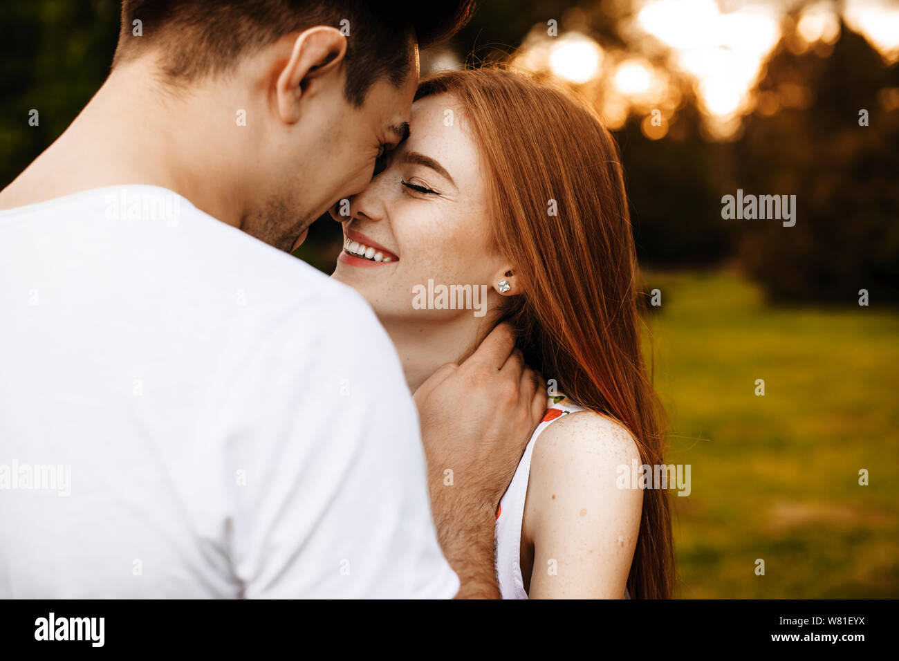 Side view portrait of a lovely couple having fun laughing while embracing with closed eyes outside against the sunset while traveling in their vacatio Stock Photo