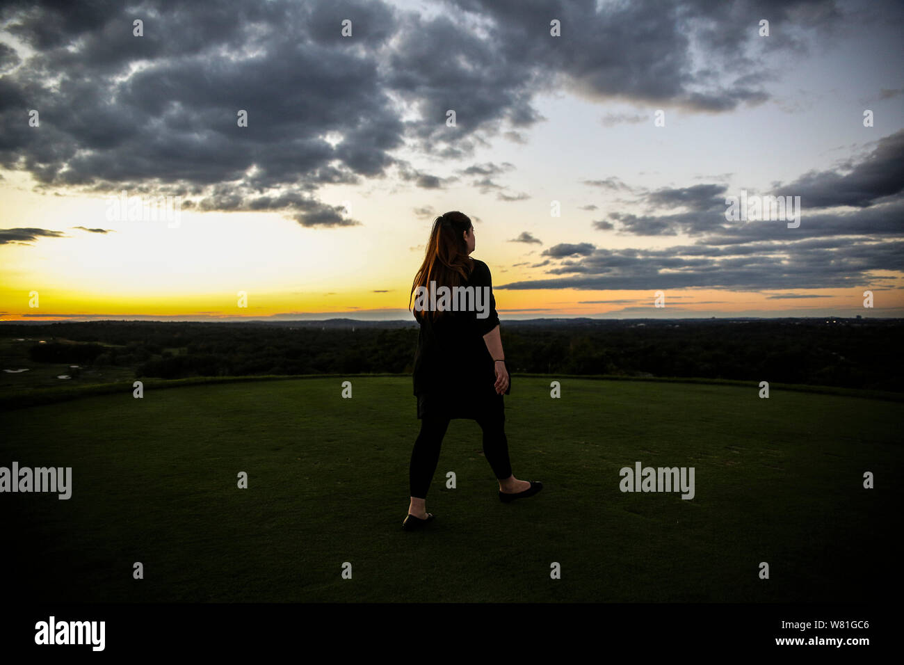 Rear View of Mid-Adult Woman on Hilltop at Sunset Stock Photo