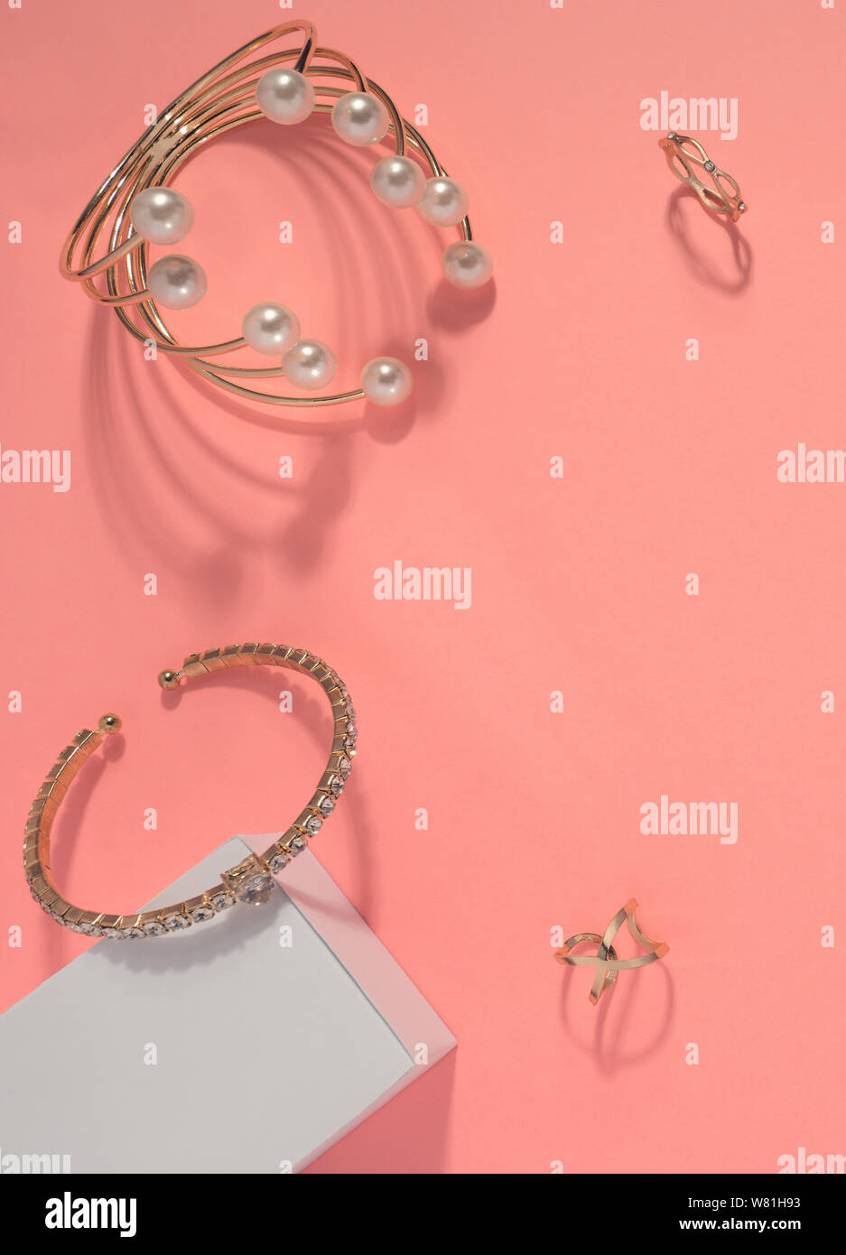 Top view of golden bracelets and golden rings on pink background Stock Photo