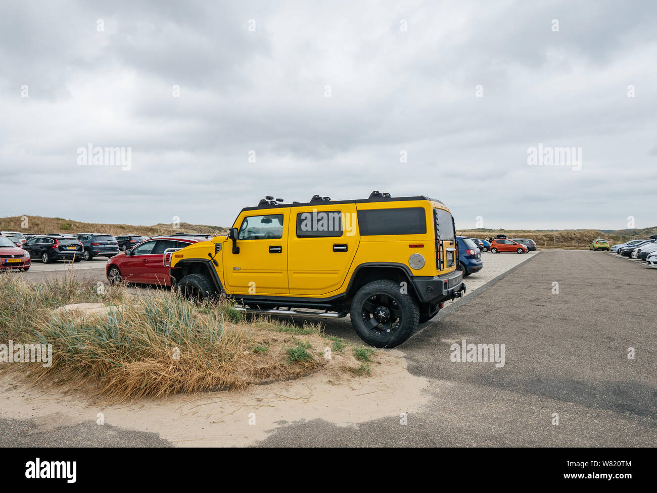 Overveen, Netherlands - Aug 16, 2019: Side view of luxury yellow hummer large SUV parked in the sand covered Dutch paid parking Stock Photo