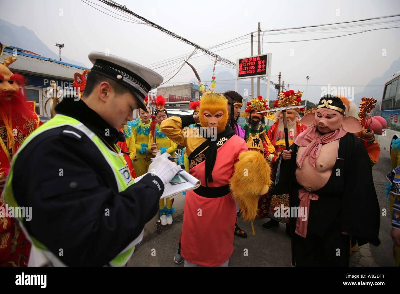 A police officer is surrounded by actors who were on their way to a "Journey to the West" performance as he checks and registers the driving license o Stock Photo