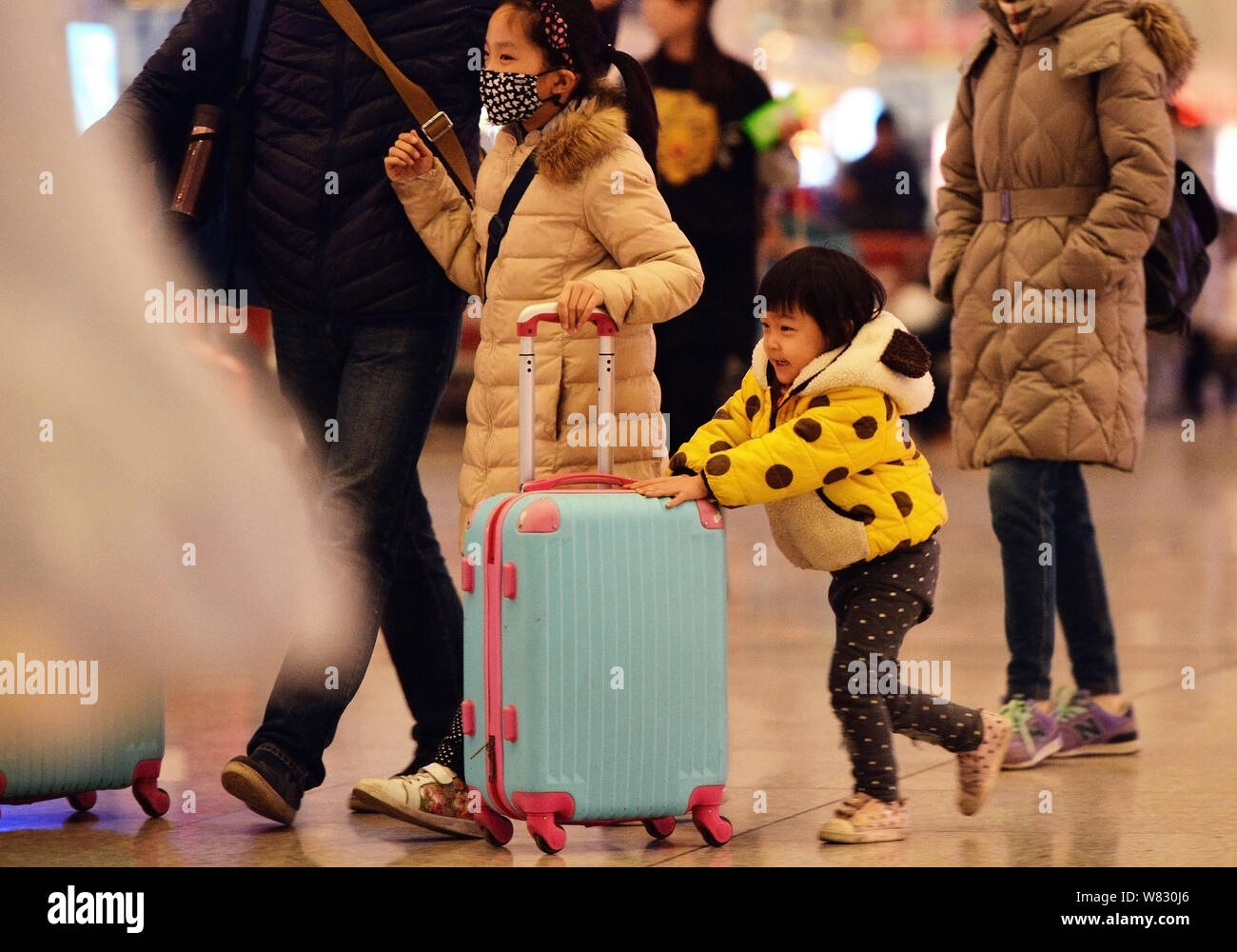 A young Chinese girl helps her elder sisiter to push suitcase as they go back home with their parents for the upcoming Chinese Lunar New Year, also kn Stock Photo