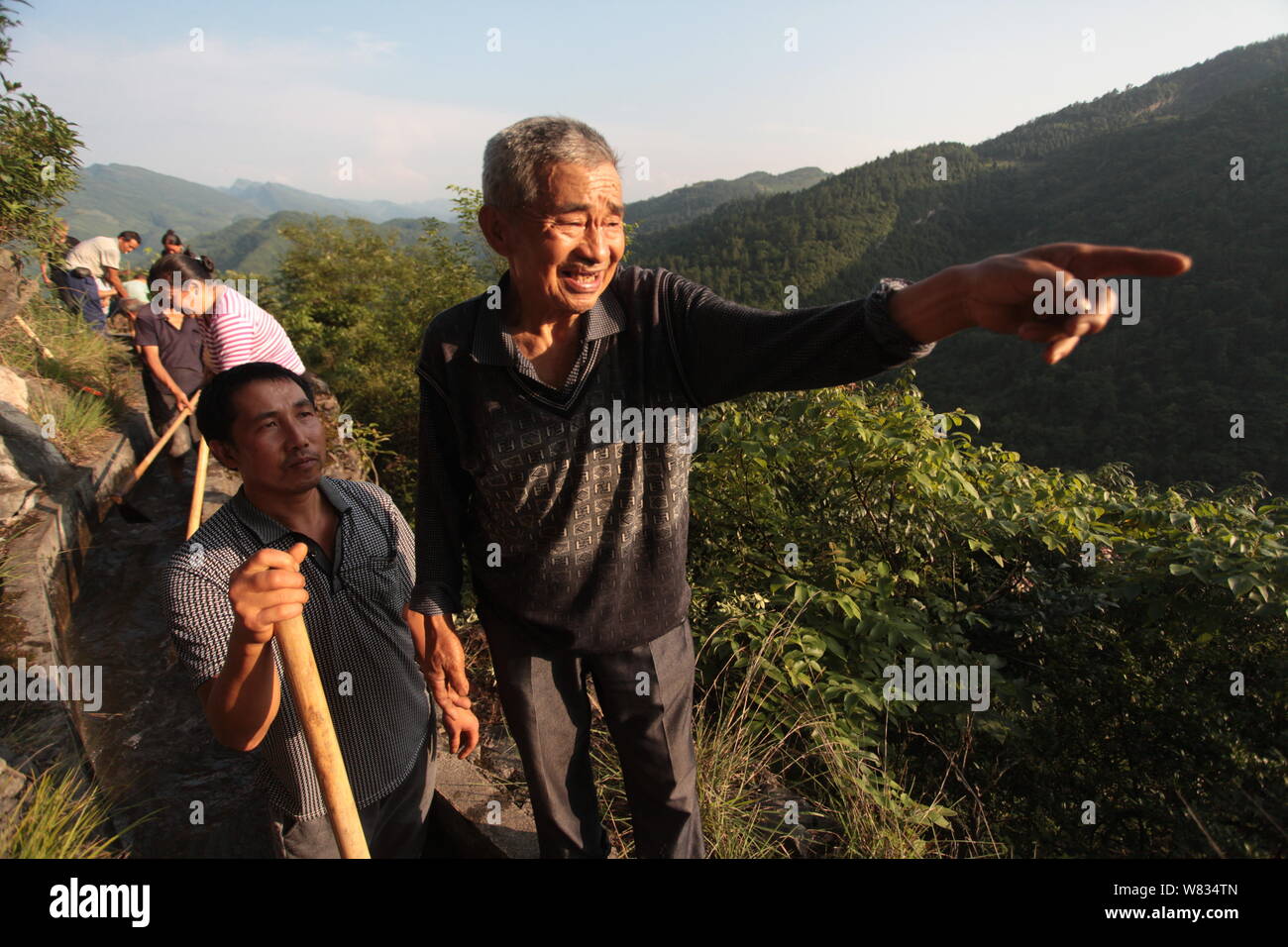 82-year-old Chinese man Huang Dafa leads local villagers to build a water channel along cliffs, stretching over seven kilometers, in Zaowangba village Stock Photo