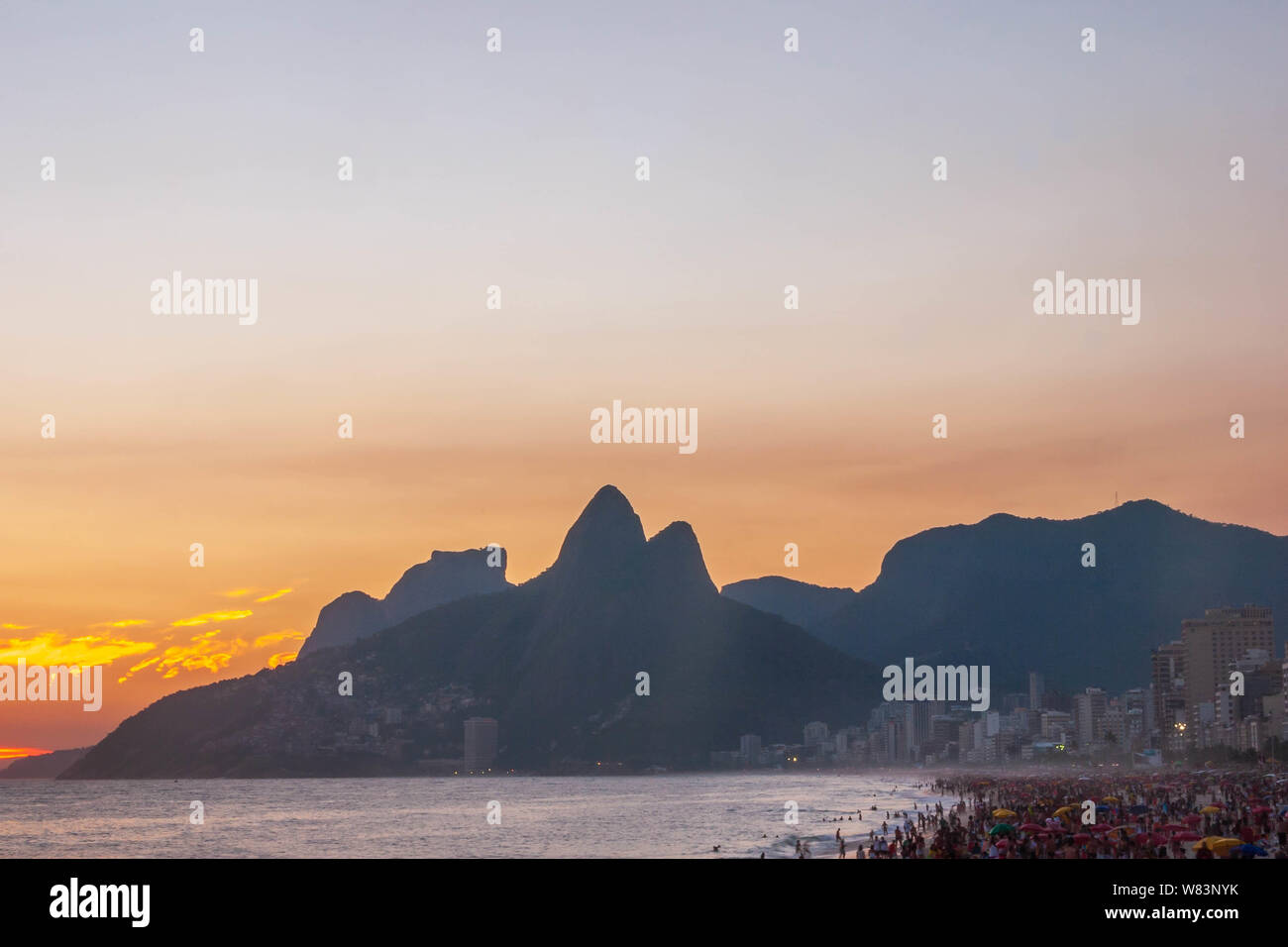 Amazing sunset at Rio de Janeiro litoral seen from Arpoador rock depicting Ipanema beach with a crowd on the sand and the silhouette of the mountains Stock Photo