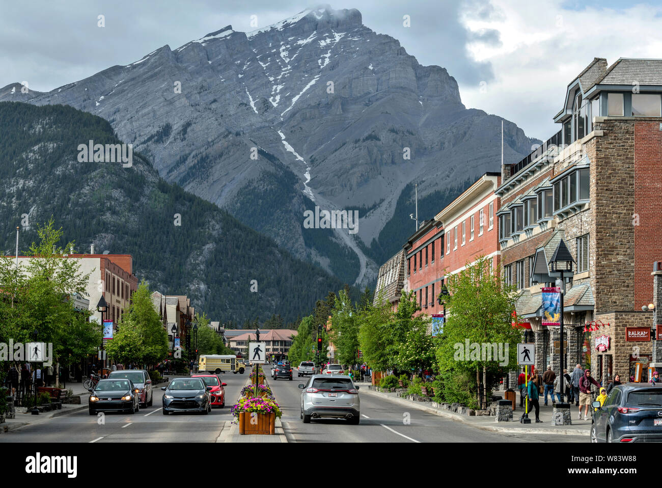 Cascade Mountain At Banff Ave - Formidable Cascade Mountain towering high at far end of busy Banff Avenue on a cloudy Spring day in Downtown Banff. Stock Photo