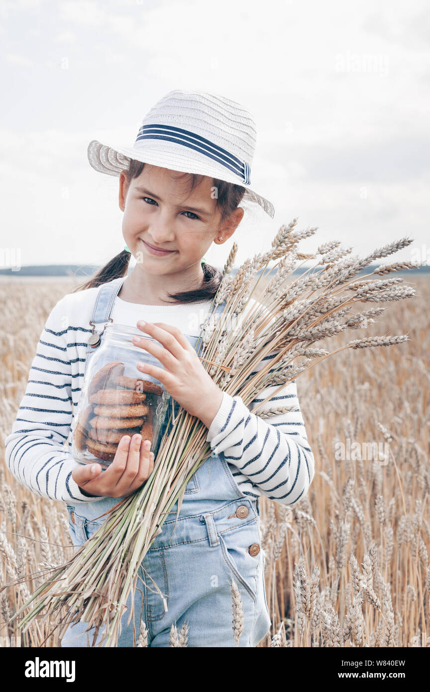 Happy little girl in a white hat on a wheat field background. Vertical shot Stock Photo