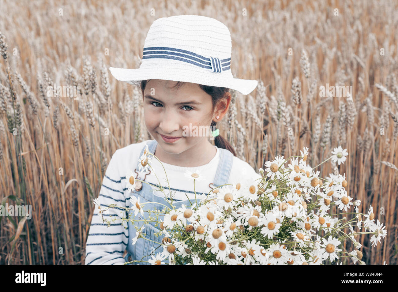 Happy cute little girl with a bouquet of daisies on a dew field