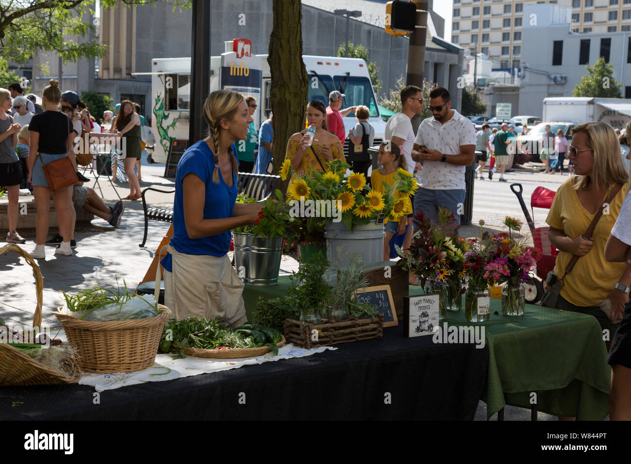 A vendor at Fort Wayne's Farmers' Market promotes her flowers to a customer in downtown Fort Wayne, Indiana, USA. Stock Photo