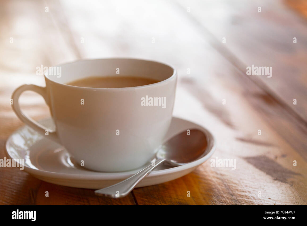 White cup of traditional indian tea masala with sauser and spon on wooden background. Sunlight toned. Stock Photo