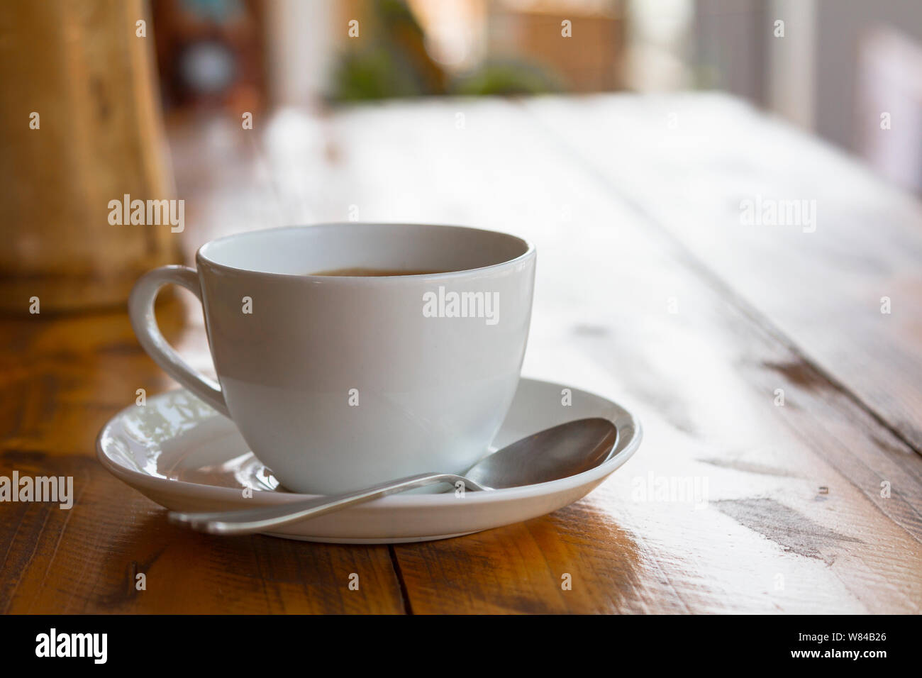 White cup of traditional indian tea masala with sauser and spon on wooden background. Stock Photo