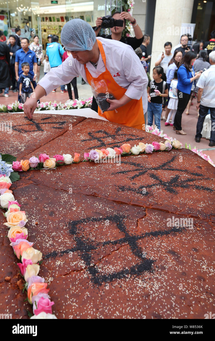 An employee from a local food company makes Chinese characters with sesame meaning "Happy Mid-Autumn Festival" on the giant mooncake with a diameter o Stock Photo